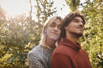 Fototapeta premium In a peaceful forest during golden hour, two young men embrace warmly surrounded by nature. Their smiles reflect joy and intimacy, showcasing a beautiful bond under soft sunlight.