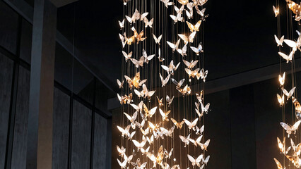 A luxurious butterfly chandelier with glowing metallic butterflies in a modern, dark architectural space.