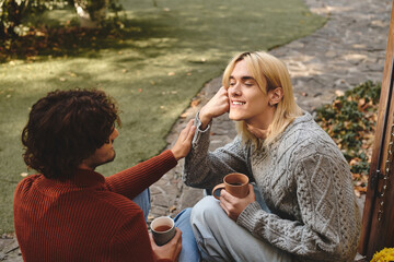 Two handsome young men enjoy each others company outdoors, sipping warm drinks.