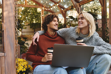 In a charming greenhouse filled with greenery and flowers, Young loving gay couple share a moment of joy while sipping coffee.