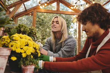 Fototapeta premium In a lively greenhouse, a young lgbt couple shares a joyful moment while tending to vibrant yellow flowers. Their smiles reflect the happiness of nurturing plants in the warm sunlight.