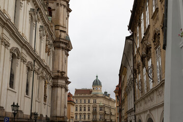 A captivating view presents a narrow street that winds charmingly between historical buildings, showcasing a prominent dome structure set against a beautifully cloudy sky