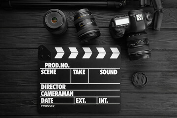 Movie clapper, camera and lens on black wooden table, flat lay