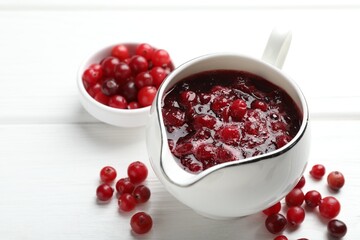 Tasty cranberry sauce in gravy boat and berries on white wooden table, closeup