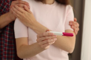 Woman with negative pregnancy test indoors, closeup. Man supporting his wife at home