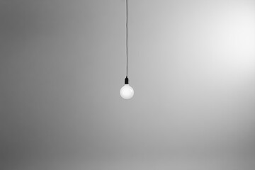 A Single Light Bulb Hanging from a Ceiling Against a Plain Grey Background