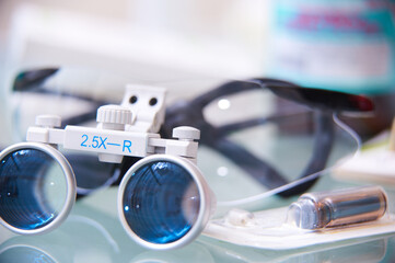 Close-up of dental or surgical loupes with magnifying lenses on a reflective surface. Professional medical equipment used for precision work.