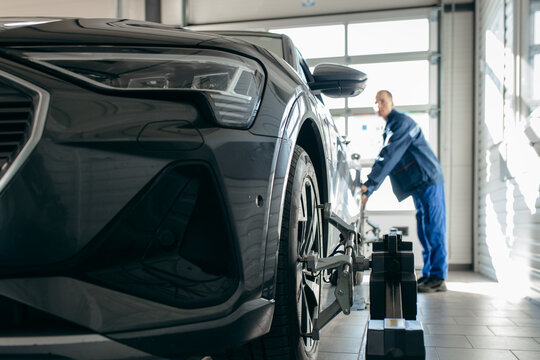 Auto mechanic installing sensor during suspension adjustment and automobile wheel alignment work at repair service station