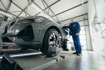 Auto mechanic installing sensor during suspension adjustment and automobile wheel alignment work at...