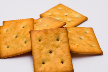 A pile of crackers on a white surface. A white cookie with a cracker on the background. Cracker cookies white background square cookie snack. A cookie with a square cookie on a lifestyle cookie.