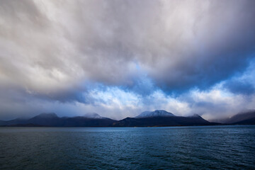 Autumn landscape of the Lyngen Alps in Northern Norway with snowy peaks, dramatic clouds, and a tranquil fjord.