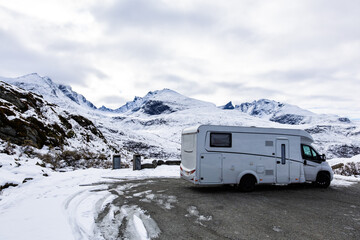 A motorhome driving along the Sognefjellsvegen road in Norway, surrounded by snow-covered mountains...