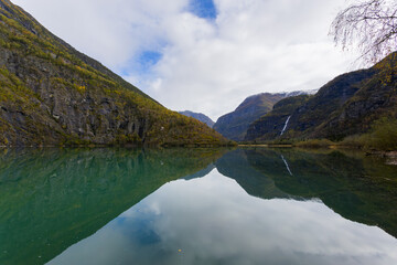 Autumn landscape in Skjolden, South Norway, with a calm lake reflecting the mountains and colorful foliage.