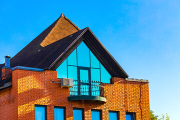 view of red brick house with glazed balcony. house with a high gable roof. brick house with attic