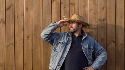 Man standing against wooden wall. Bearded. 40-45 years old. Dressed in denim jacket. Outdoors....
