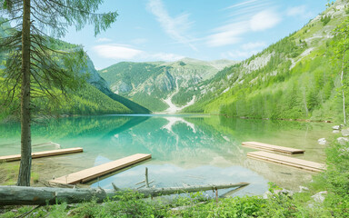 natural landscape featuring a pristine lake surrounded by lush greenery. A wooden footbridge arches gracefully over the water