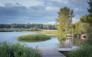natural landscape featuring a pristine lake surrounded by lush greenery. A wooden footbridge arches gracefully over the water
