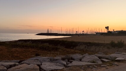 Sunset on the coast next to the harbor, with the sky illuminated by warm tones, creating a calm and serene ambiance © Karen Images