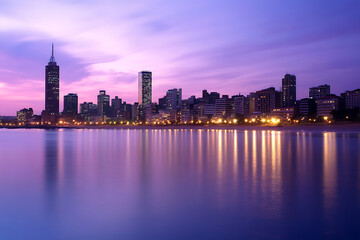 Obraz premium Coastal City Skyline at Dusk: Vibrant Reflections and City Lights