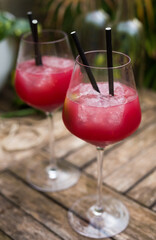 Red cocktail with ice in glass with stem on wooden surface