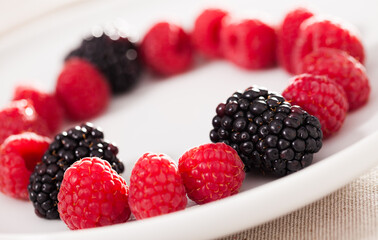Raspberries and blackberries laid out on a white plate in circle