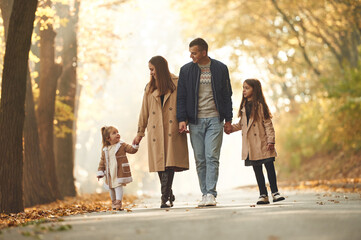 Weekend walk. Happy family of mother, father and two daughters are in the autumn park, forest, road