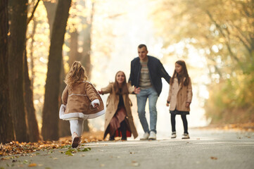 Weekend walk. Happy family of mother, father and two daughters are in the autumn park, forest, road