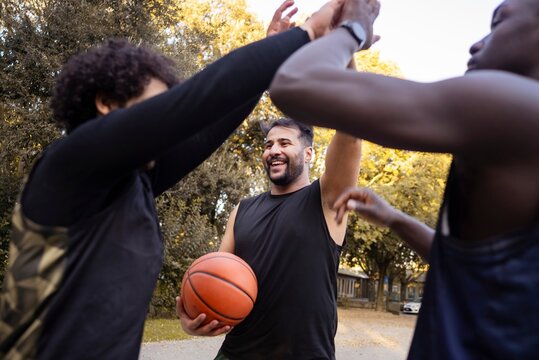 A group of basketball players smiling and high-fiving each other after a game on an outdoor park court surrounded by lush trees and a peaceful setting