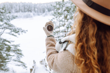 Woman holding a navigational compass on background of a snowy winter forest. Concept of direction, orientation, travel.