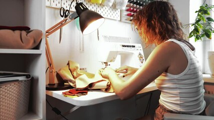 Woman, developing sewing skills, sewing on sewing machine, creating comfortable clothes. Learns art of sewing in equipped work place at table. Concept of learning basics of creating clothes and sew