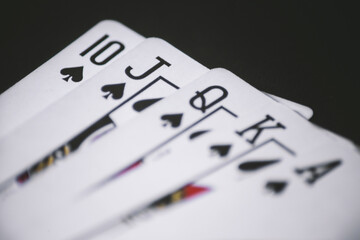 close-up of a royal flush in spades, elegantly arranged on a matte black surface. The dark background enhances the contrast, while soft lighting highlights the sharp details and intricate design of th