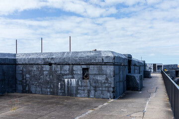 A weathered concrete fort wall with iron loops, surrounded by an elevated pathway and set under a...