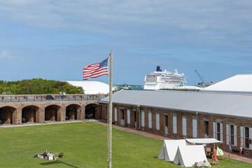 An American flag waves near a historic brick fort in Key West, with a cruise ship and coastal...