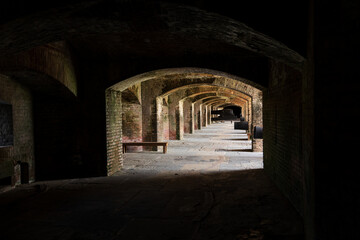 Obraz premium Historical brick fort with arched corridors, antique cannons, and weathered structures, showcasing intricate masonry and military architecture under natural light.