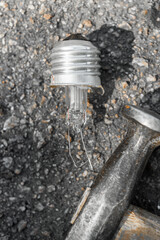 Closeup photo of hammer and destroyed electric light bulb, Destroyed incandescent lamp showing significant damage, glass shards spread around