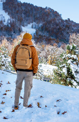 rear view of a man in a red jacket and hat with a yellow backpack admiring a beautiful mountain view with an autumn-winter forest landscape Hiking and tourism