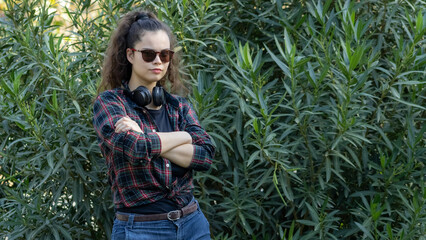 Young white girl in casual clothes with headphones in a green park acts rude