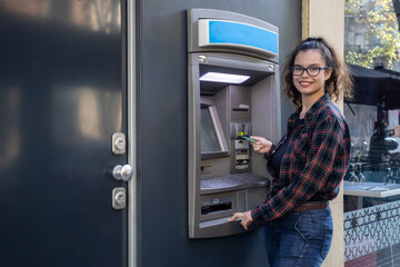 Young white girl withdraws money from an ATM while posing with her credit card