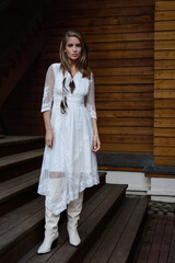 A young girl poses in a boho wedding dress, cowboy boots, a cowboy hat, and a denim jacket.