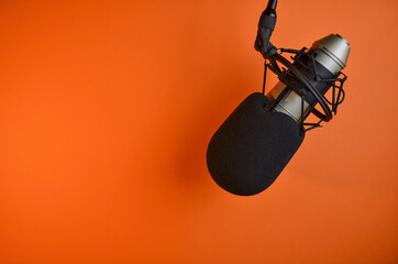 Professional microphone hanging on an orange background ready for recording or broadcasting