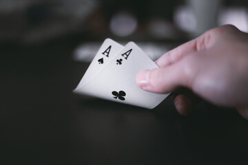 A pair of black aces on a poker table. A young man lifts the cards, bending them slightly to reveal...