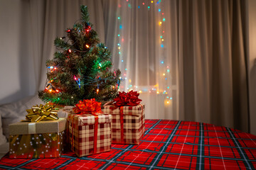 Decorative Christmas tree surrounded by colorful gifts on a festive table with twinkling lights in a cozy indoor setting