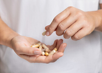 Woman holding in hands beige medical herbal capsules closeup over white shirt
