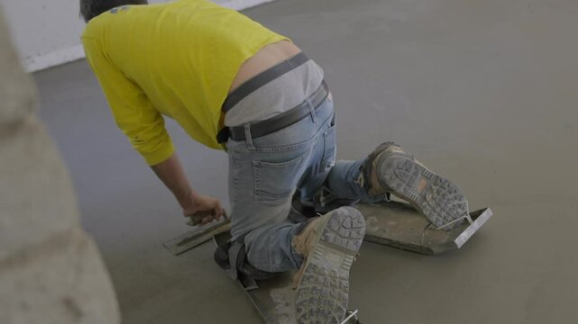 This video shows a rear view of a cement worker using trowel to smooth out floor.