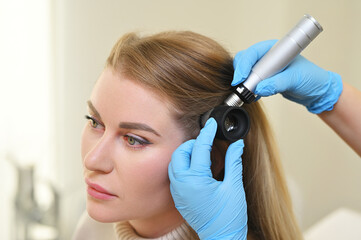 Fototapeta premium dermatologist trichologist examines the hair structure of a young woman's patient using an optical dermatoscope device.