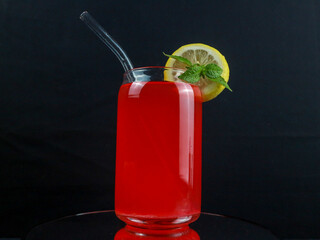 A glass of red drink with a mint leaves and orange on top, black background