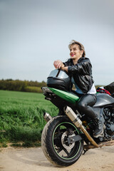 Obraz premium A woman is sitting on a motorcycle with a helmet on. She is wearing a leather jacket and black pants. The motorcycle is parked on a dirt road