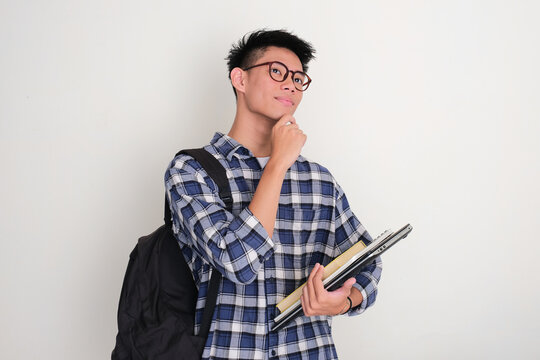 Indonesian college student wearing backpack dreaming about something while holding books and laptop