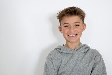 cool young 12 year old boy with grey hoody sweater posing in front of white background, having fun