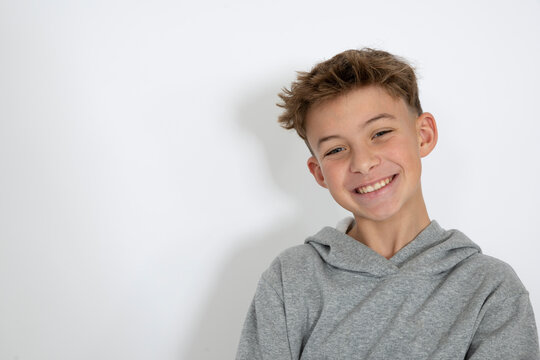 cool young 12 year old boy with grey hoody sweater posing in front of white background, having fun